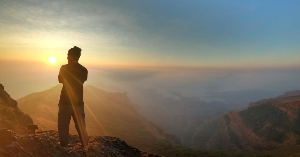 Person standing on mountain at sunrise.