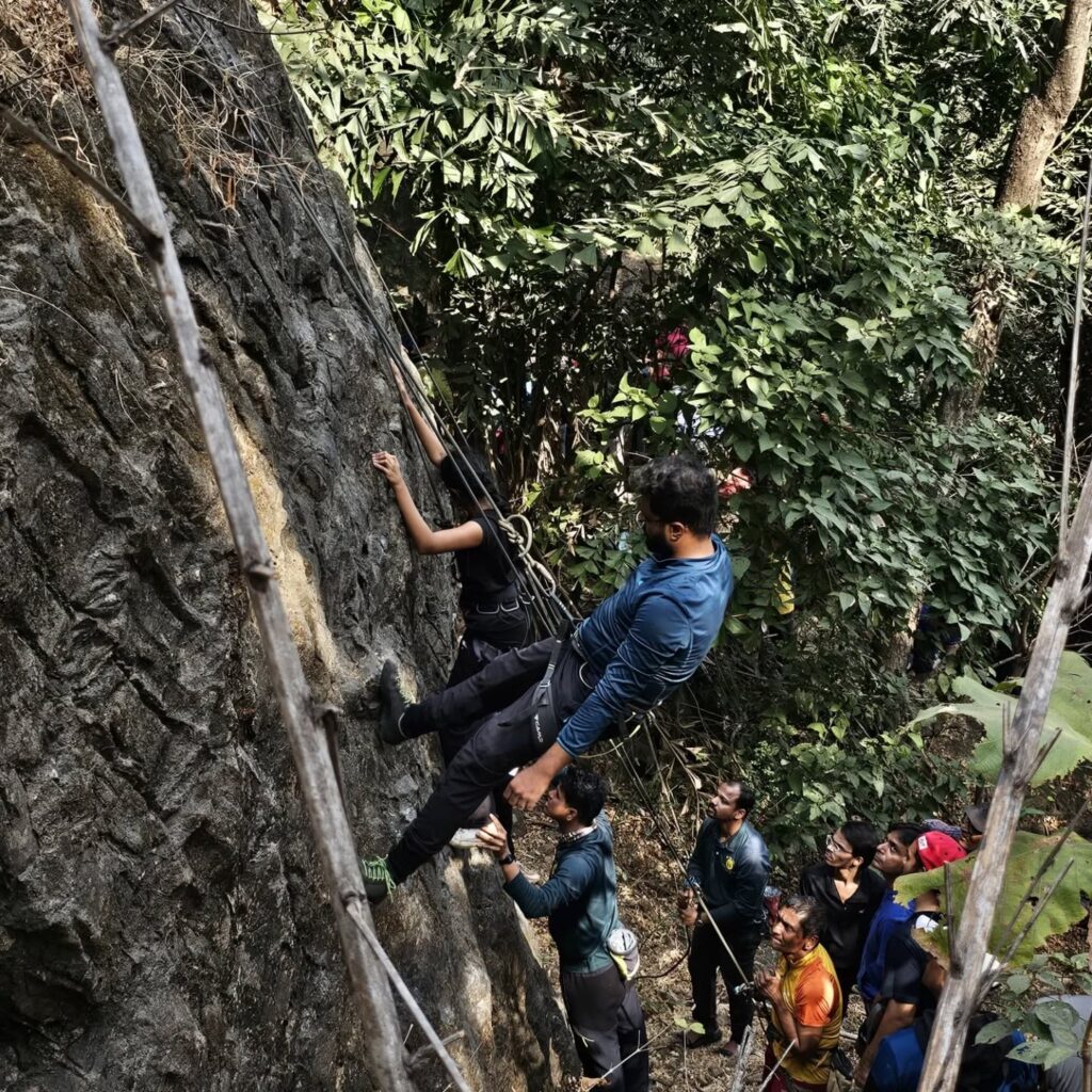 People rock climbing with safety gear in forest area.