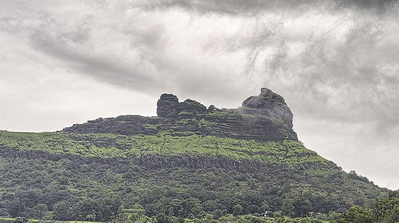 Green hill with cloudy sky and unique rock formation.