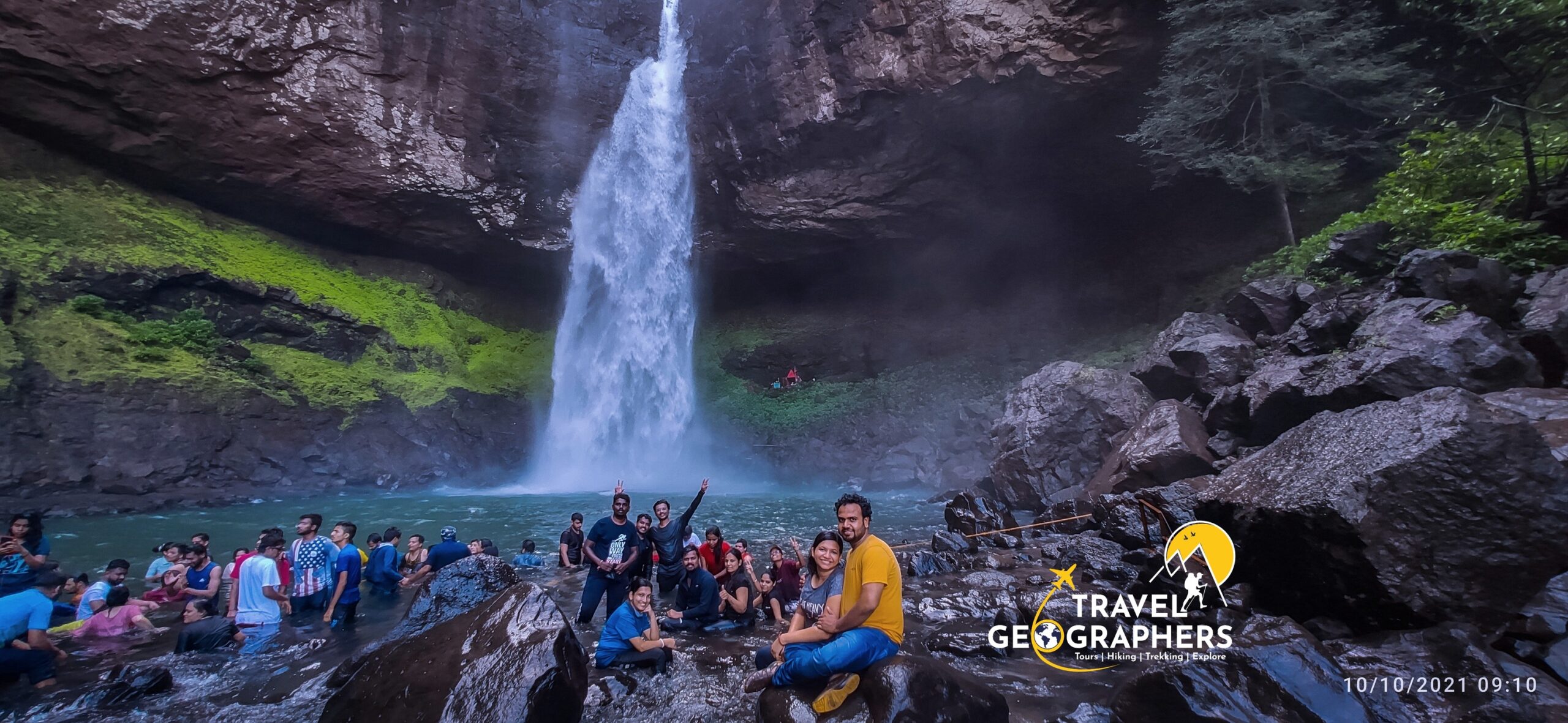 People enjoying waterfall in rocky green landscape.