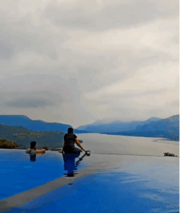 Two people in infinity pool overlooking scenic lake view.