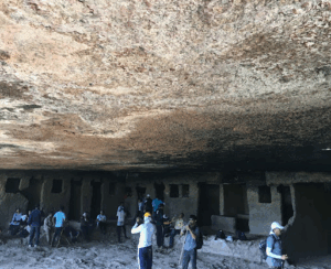 Group exploring ancient cave dwellings, rocky ceiling visible.