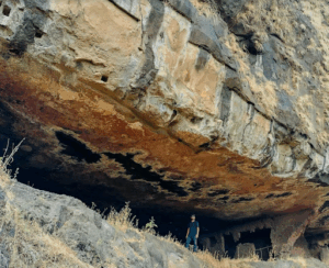 Person standing under large rocky cave entrance.