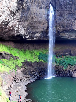 Tall waterfall flowing into rocky green pond.